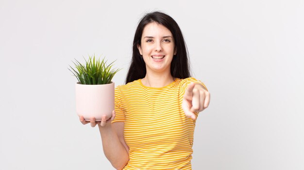 Jolie femme pointant sur la caméra vous choisissant et tenant une plante décorative