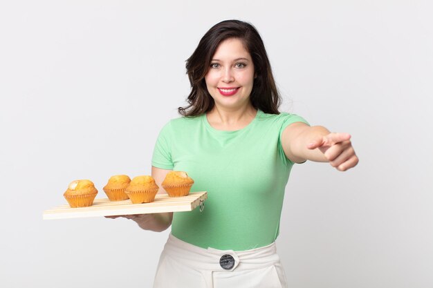 Jolie femme pointant sur la caméra vous choisissant et tenant un plateau à muffins