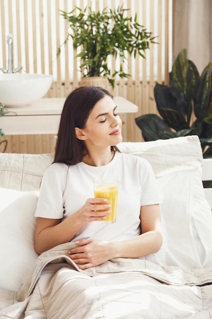 Jolie femme portant un t-shirt buvant du jus d'orange au lit