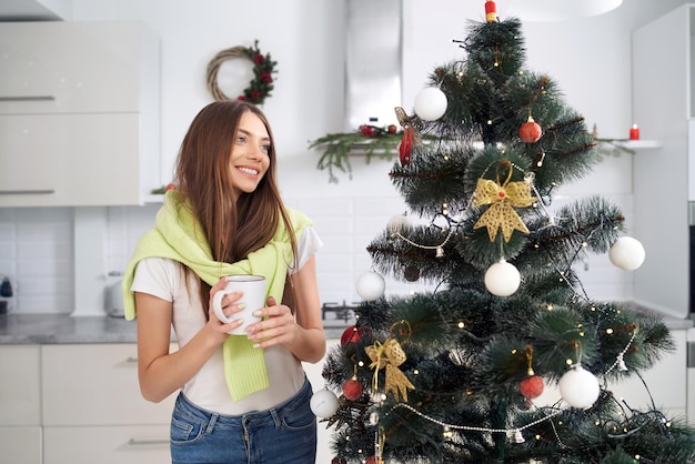 Jolie femme près de l'arbre de Noël dans la cuisine