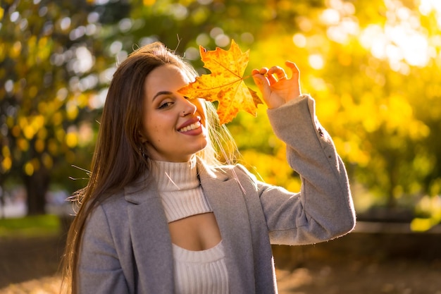 Une jolie femme profitant de l'automne dans un parc au coucher du soleil avec une feuille sur son visage