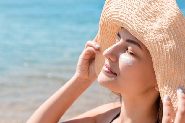 Jolie femme protège sa peau sur le visage avec un écran solaire à la plage.