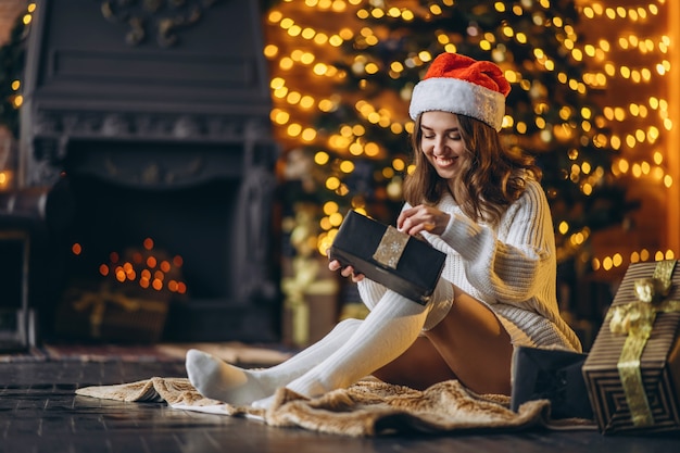 Jolie femme en pull chaud, chaussettes et chapeau de Noël, assise sur le sol