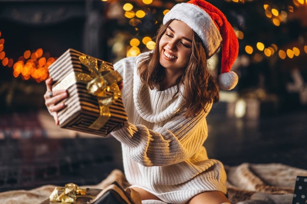 Jolie femme en pull chaud, chaussettes et chapeau de Noël, assise sur le sol