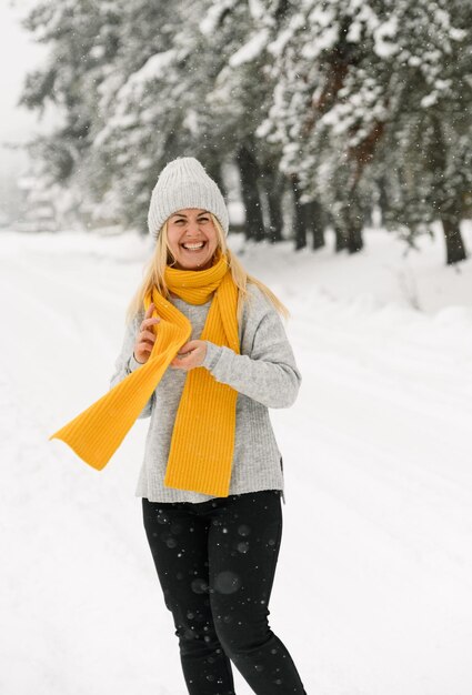 Jolie femme en pull gris et écharpe jaune marche dans une chute de neige. Femme s'amusant dans la forêt d'hiver. Portrait en plein air de la beauté blonde lady posing in wood