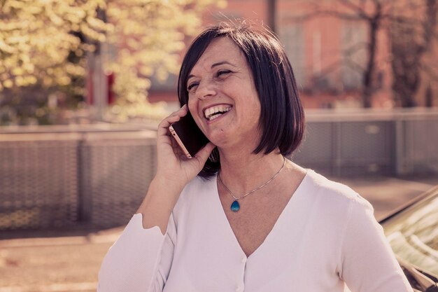 Une jolie femme qui parle et rit avec son smartphone à l'extérieur.