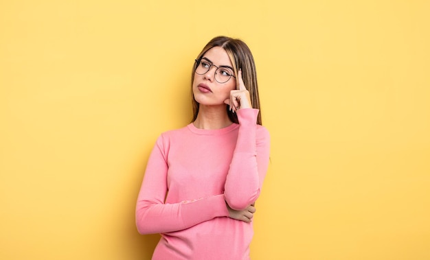 Jolie femme de race blanche avec un regard concentré, se demandant avec une expression douteuse, levant les yeux et sur le côté