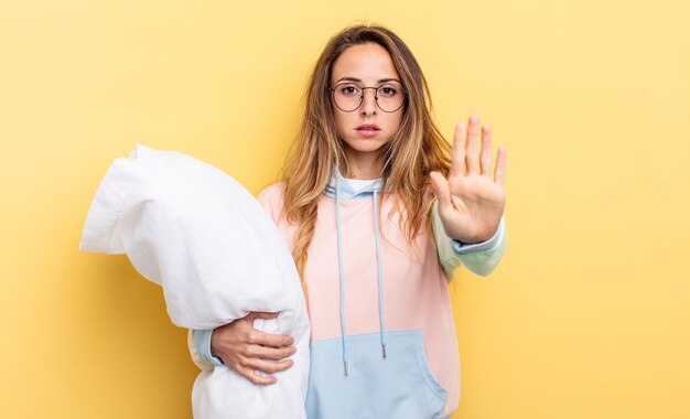 Jolie femme à la recherche sérieuse montrant la paume ouverte faisant un geste d'arrêt. notion de pyjama