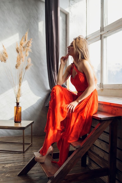 Jolie femme en robe de soirée avec une coiffure posant près d'un bar-restaurant regardant à huis clos