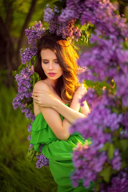 jolie femme en robe verte posant près de décor de fleurs lilas.