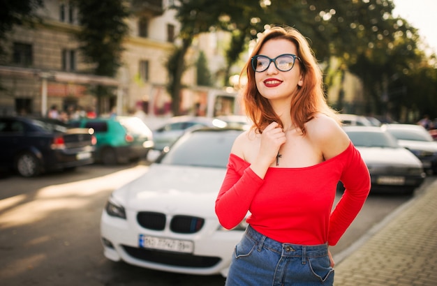 Jolie femme rousse aux lunettes portant une blouse rouge