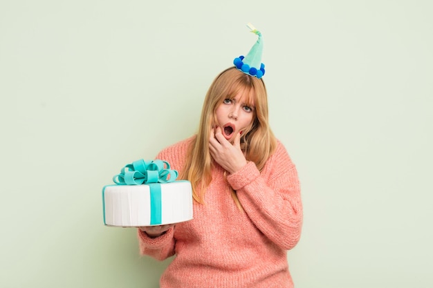 Jolie femme rousse avec la bouche et les yeux grands ouverts et la main sur le concept d'anniversaire du menton