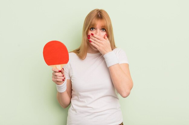 Jolie femme rousse couvrant la bouche avec les mains avec un concept de ping-pong choqué