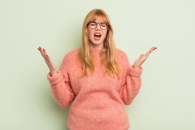 Jolie femme rousse criant furieusement stressée et agacée avec les mains en l'air en disant pourquoi moi