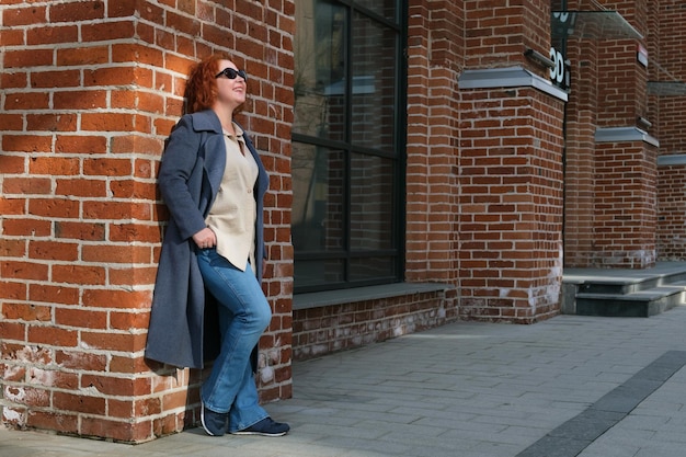 Jolie femme rousse dans un manteau bleu se tient à l'extérieur d'un bâtiment en brique