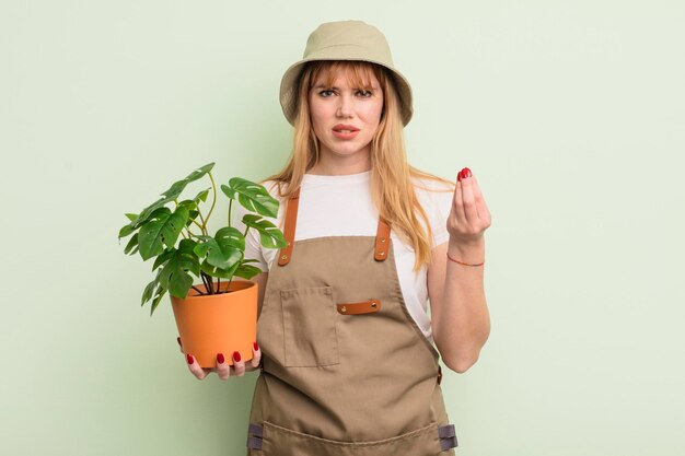 Jolie femme rousse faisant un capice ou un geste d'argent, vous disant de payer. notion de jardinier