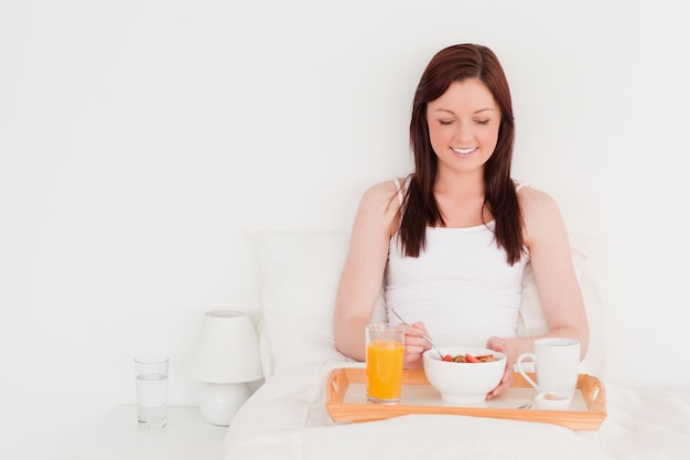 Jolie femme rousse prenant son petit déjeuner assis sur son lit