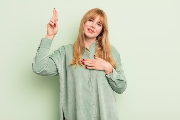 Jolie femme rousse qui a l'air heureuse, confiante et digne de confiance, souriante et montrant le signe de la victoire avec une attitude positive