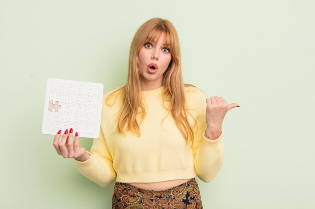 Jolie femme rousse à la recherche d'un concept de puzzle incomplet incrédule