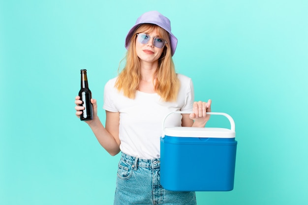 Jolie femme rousse avec un réfrigérateur portable et une bière