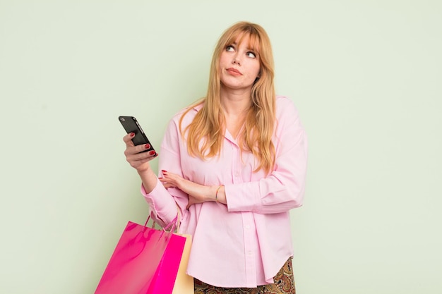 jolie femme rousse avec des sacs à provisions et un smartphone