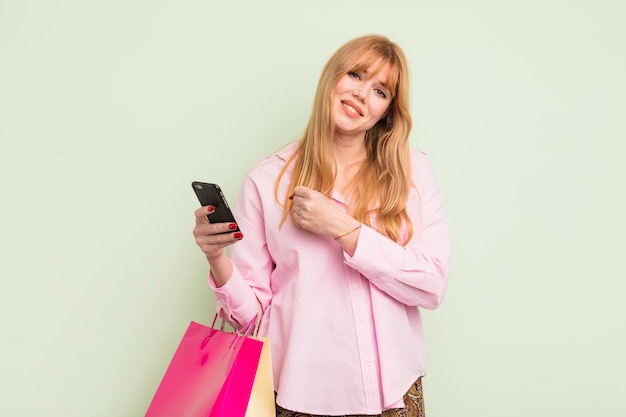 Jolie femme rousse avec des sacs à provisions et un smartphone