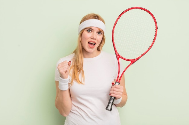 Jolie femme rousse se sentant choquée en riant et célébrant le concept de tennis de succès