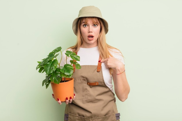 Jolie femme rousse se sentant heureuse et pointant vers soi avec un concept de jardinier excité