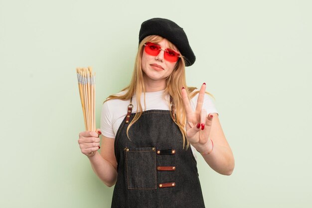 Jolie femme rousse souriante et amicale montrant l'artiste numéro deux avec le concept de pinceaux