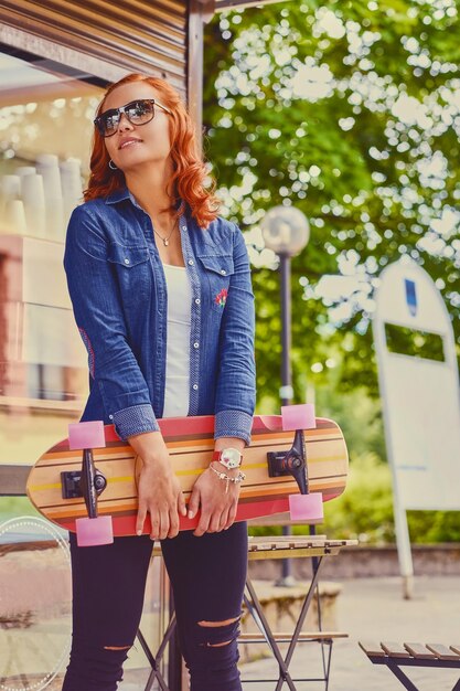 La jolie femme rousse tient un longboard.