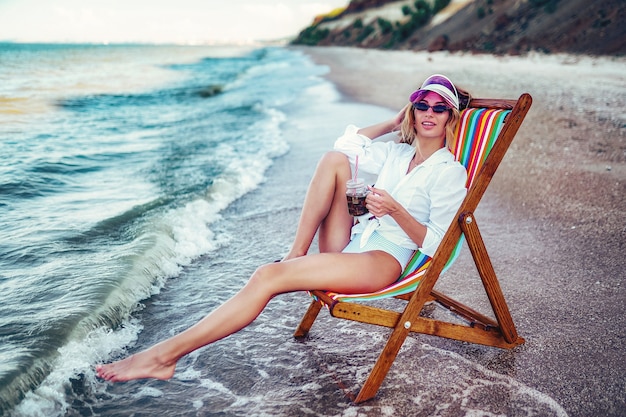 Jolie femme se détendre sur une plage de transats et boit de l'eau gazeuse