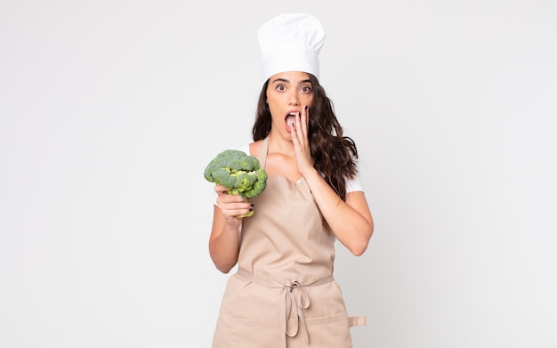 Jolie femme se sentant choquée et effrayée portant un tablier et tenant un brocoli