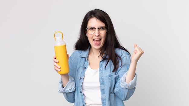 Jolie femme se sentant choquée, riant et célébrant le succès et tenant un thermos de café