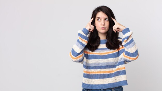 Jolie femme se sentant confuse ou doutant de se concentrer sur une idée en réfléchissant fort en cherchant à copier l'espace sur le côté