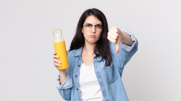 Jolie femme se sentant croisée, montrant les pouces vers le bas et tenant un thermos à café