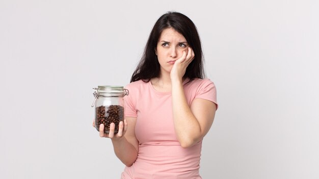 Jolie femme se sentant ennuyée, frustrée et endormie après une fatigue et tenant une bouteille de grains de café