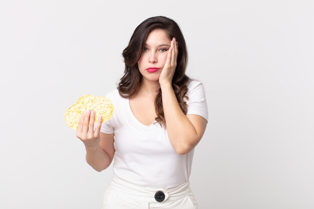 Jolie femme se sentant ennuyée, frustrée et somnolente après une fatigue et tenant des gâteaux de riz diététiques