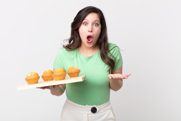 Jolie femme se sentant extrêmement choquée et surprise et tenant un plateau à muffins