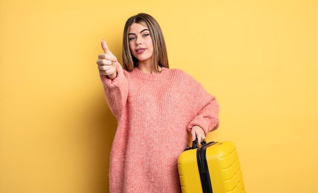 Jolie femme se sentant fière, souriant positivement avec les pouces vers le haut. concept de voyage valise