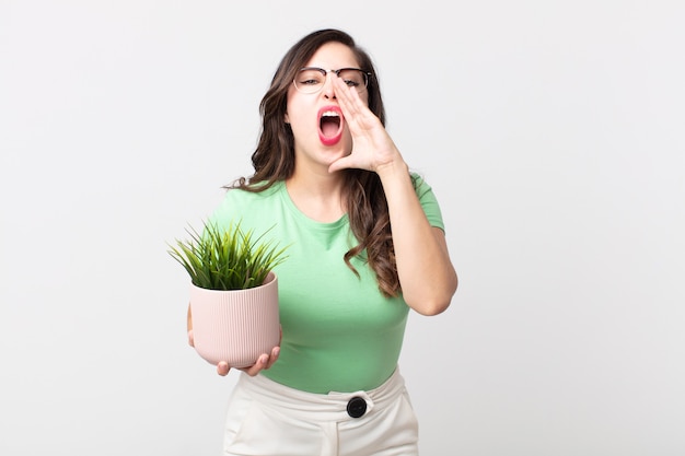 Jolie femme se sentant heureuse, donnant un grand cri avec les mains à côté de la bouche et tenant une plante décorative