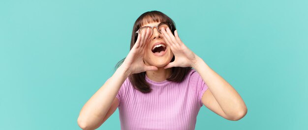 Jolie femme se sentant heureuse, excitée et positive, donnant un grand cri avec les mains à côté de la bouche, appelant