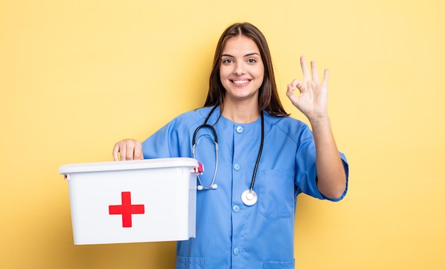 Jolie femme se sentant heureuse de montrer son approbation avec une infirmière de geste correct avec une infirmière de trousse de premiers soins