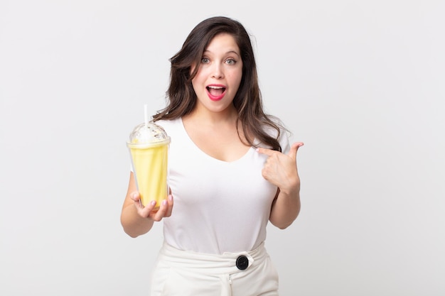 Jolie femme se sentant heureuse et pointant vers soi avec un excité et tenant un milkshake à la vanille