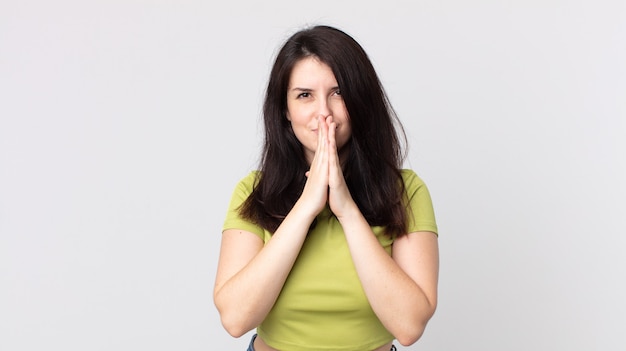 Jolie femme se sentant inquiète, pleine d'espoir et religieuse, priant fidèlement avec les paumes pressées, implorant le pardon