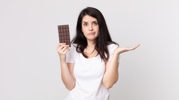 Jolie femme se sentant perplexe et confuse et doutant et tenant une barre de chocolat