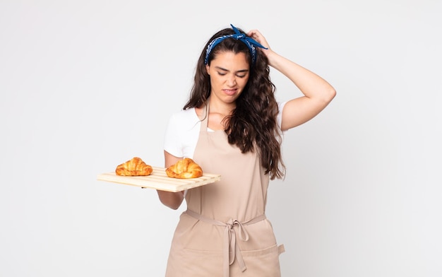 Photo jolie femme se sentant perplexe et confuse, se grattant la tête et tenant un plateau de croissants