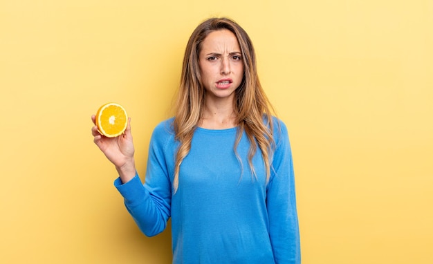 Jolie femme se sentant perplexe et confuse tenant la moitié d'orange