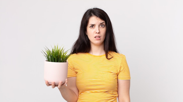 Jolie femme se sentant perplexe et confuse et tenant une plante décorative
