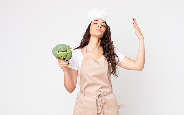 Jolie femme se sentant stressée, anxieuse, fatiguée et frustrée portant un tablier et tenant un brocoli