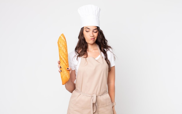 Jolie femme se sentant triste, bouleversée ou en colère et regardant sur le côté portant un tablier et tenant une baguette de pain